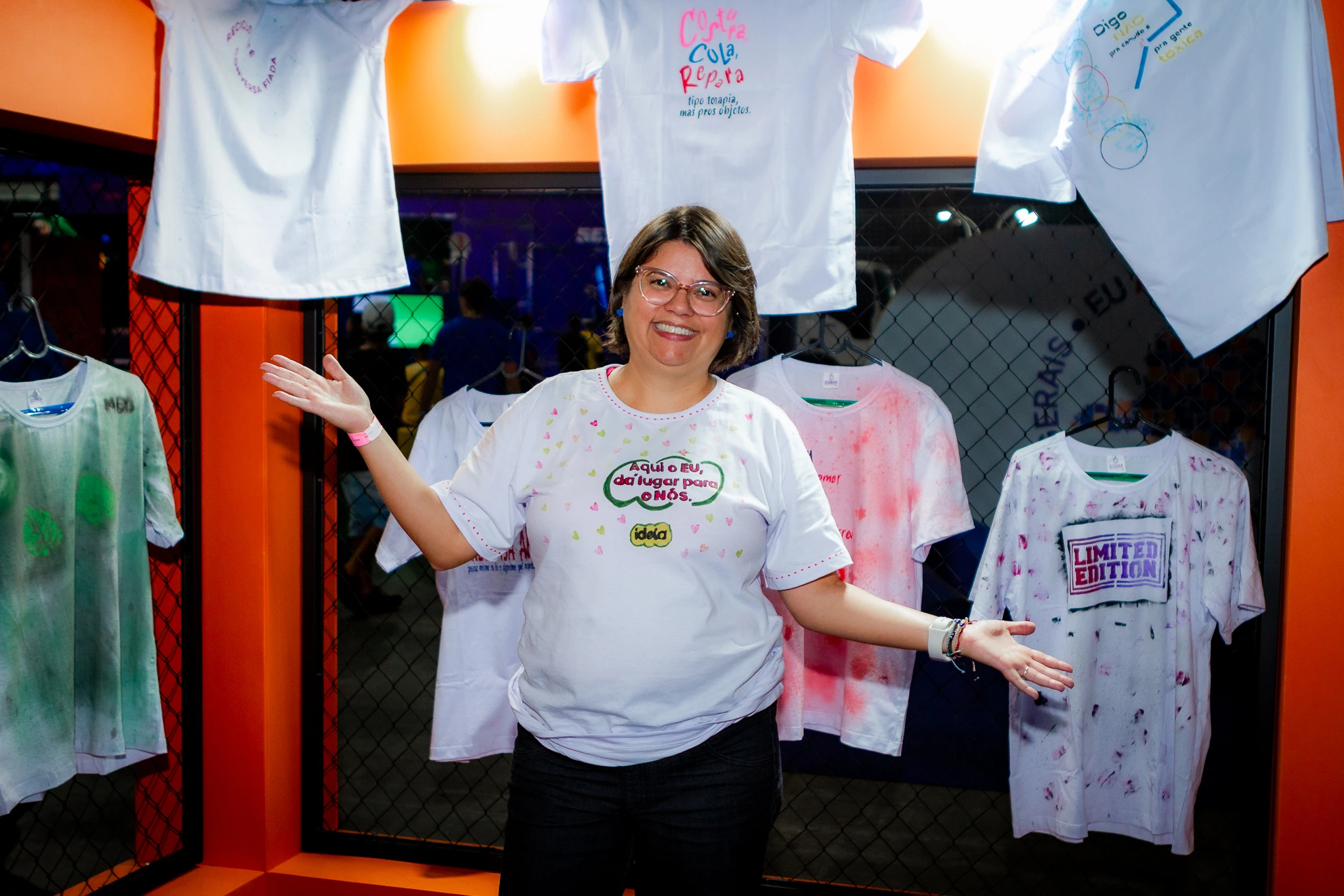 Andreia, mulher e fundadora da Ideia Negocios do Bem mostrando o stand do sesc na semana S com customizacao de camisetas