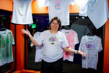 Andreia, mulher e fundadora da Ideia Negocios do Bem mostrando o stand do sesc na semana S com customizacao de camisetas